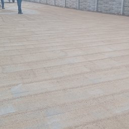 P.H.U. Węglewscy - Przygotowanie terenu pod kostkę brukową: wyrównane podłoże z piasku, widoczne ślady po zagęszczarce, schody wejściowe z boku, fragment betonowego ogrodzenia w tle.