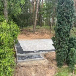 P.H.U. Węglewscy - Ułożona kostka brukowa w leśnym otoczeniu, z obrzeżami z ciemnej kostki i schodami. Widoczne drzewa i krzewy, świeżo wykończona nawierzchnia.