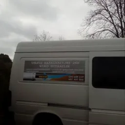 Biały samochód dostawczy z reklamą usług kanalizacyjnych WUKO HYDRAULIK 24H, widoczne numery telefonów