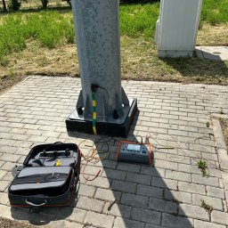 Energomontaż mgr inż. Zdzisław Adamczyk - Pomiar uziemienia słupa oświetleniowego specjalistycznym miernikiem. Otwarta torba narzędziowa obok.