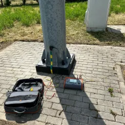 Pomiar uziemienia słupa oświetleniowego specjalistycznym miernikiem. Otwarta torba narzędziowa obok.