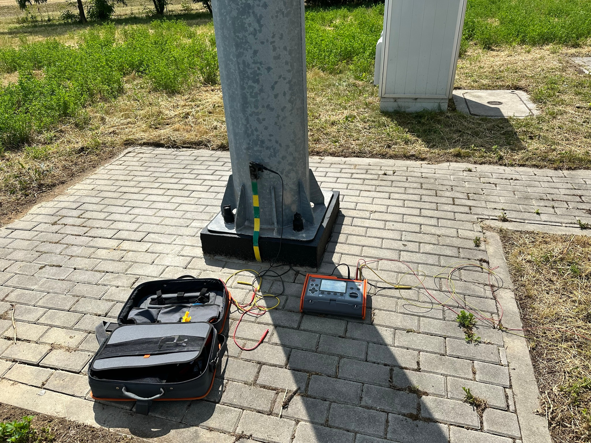Pomiar uziemienia słupa oświetleniowego specjalistycznym miernikiem. Otwarta torba narzędziowa obok.