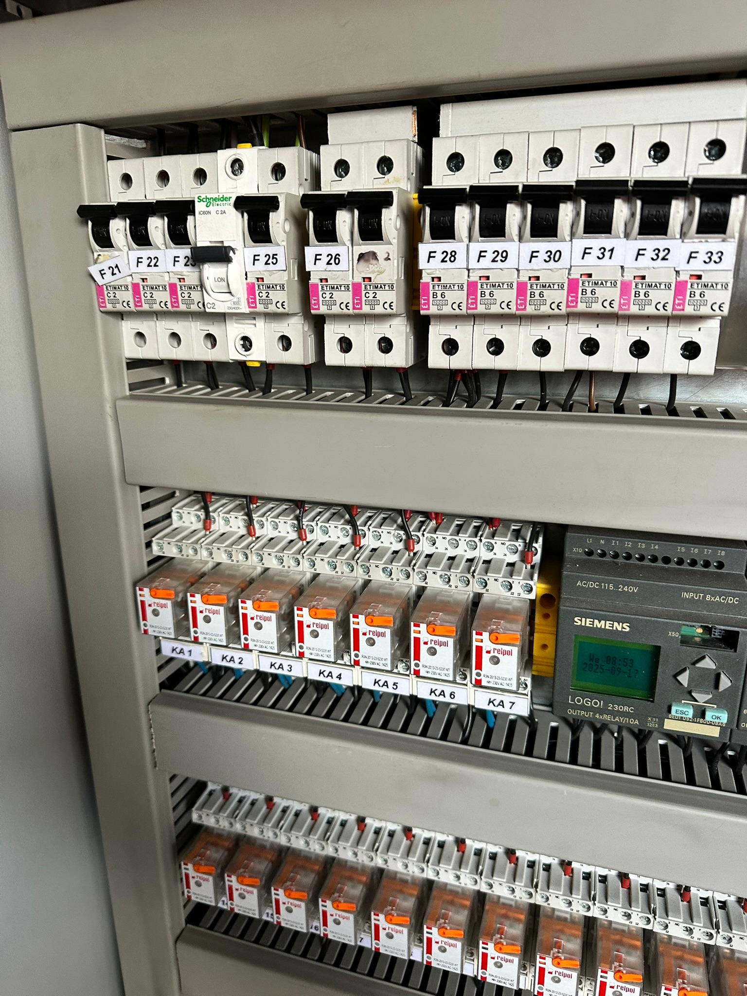 Szczegółowe ujęcie rozdzielnicy elektrycznej z bezpiecznikami, przekaźnikami i modułem sterującym Siemens LOGO!, ukazujące złożoność instalacji.