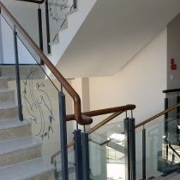 METAL-STYL CONSTRUCTION BARBARA CEGIELSKA-CIEŚLA - Szklane balustrady schodowe z drewnianą poręczą i dekoracyjnym motywem na szkle, widok z dołu, jasne wnętrze.