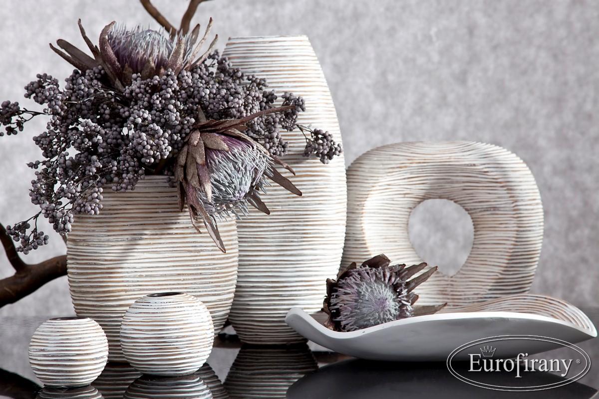 Kompozycja dekoracyjna z suszonych kwiatów i gałązek w wazonach o prążkowanej fakturze, uzupełniona ceramiczną rzeźbą w kształcie obwarzanka i podłużnym naczyniem, całość na czarnym, błyszczącym...