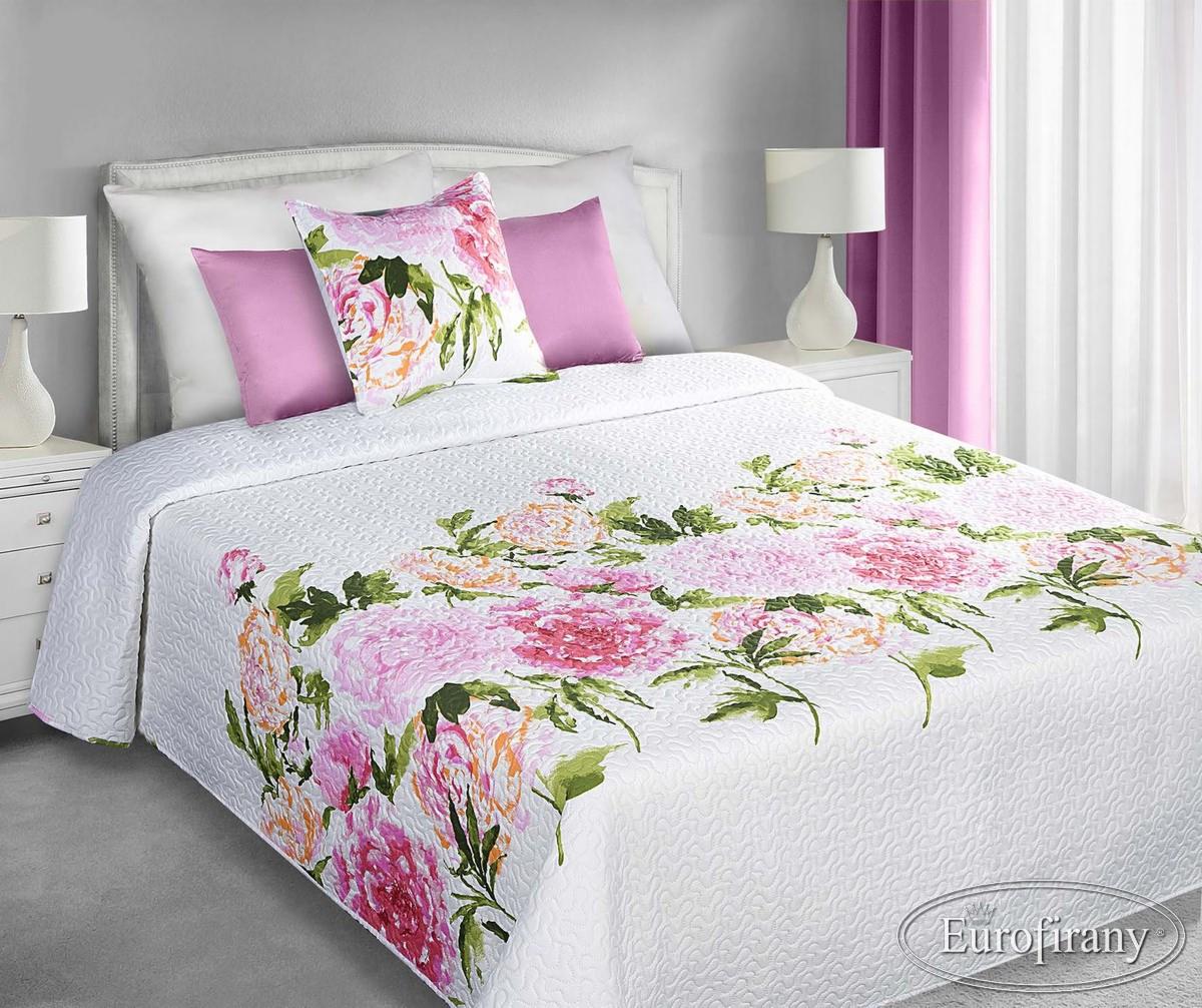 Biała, pikowana narzuta na łóżko z motywem różowych kwiatów, dopasowane poduszki i zasłony w tle.