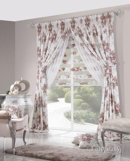 Eleganckie, długie zasłony w kwiaty, z białymi, zwiewnymi firankami, upięte po bokach, na tle okna z widokiem na ogród, z dopasowaną poduszką i dywanem.