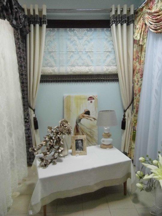 Dekoracyjna aranżacja okna z zasłonami w różnych stylach i roletą rzymską, uzupełniona o lampkę nocną i ramkę ze zdjęciem na stoliku.