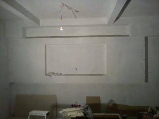 Wnętrze w trakcie przygotowania do prac wykończeniowych: surowe ściany z widocznymi elementami instalacji elektrycznej, częściowo zabezpieczone podłoże, widoczne narzędzia i materiały budowlane.