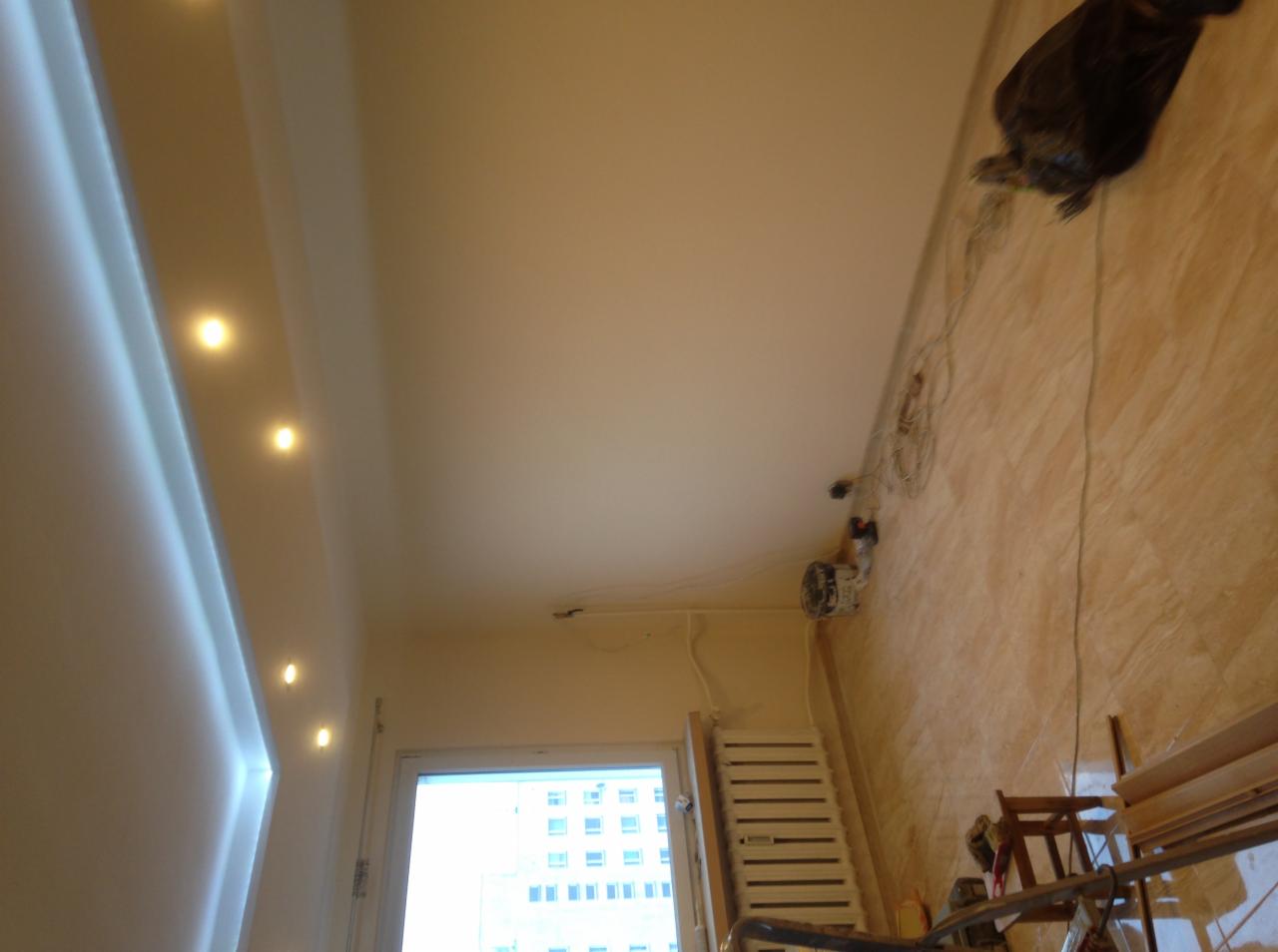 Biały sufit z oświetleniem punktowym LED, widoczne narzędzia i przewody na ścianie, okno z widokiem na budynek w tle.