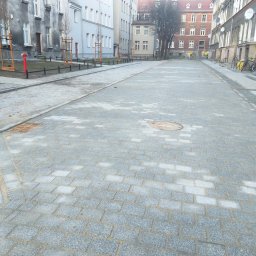 Walec sp zo.o. - Nowa, jasnoszara kostka granitowa na ulicy miejskiej z hydrantem i młodymi drzewkami. Widok perspektywiczny w kierunku zabudowy.