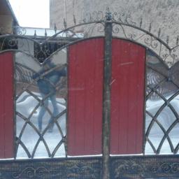 Usługi  Ślusarsko-Instalacyjne Kłos Zdzisław - Kute, dwuskrzydłowe ogrodzenie z elementami drewnianymi pomalowanymi na czerwono, widoczne płatki śniegu.