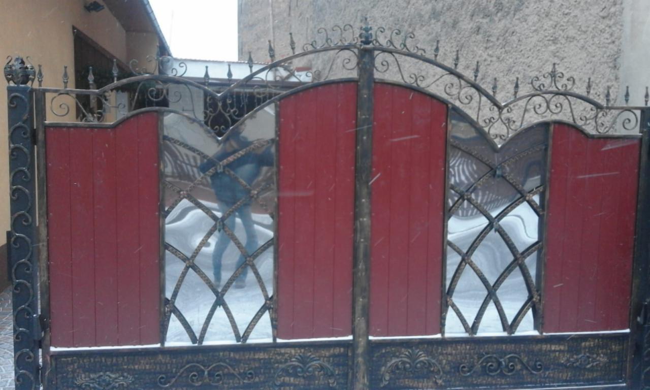 Kute, dwuskrzydłowe ogrodzenie z elementami drewnianymi pomalowanymi na czerwono, widoczne płatki śniegu.