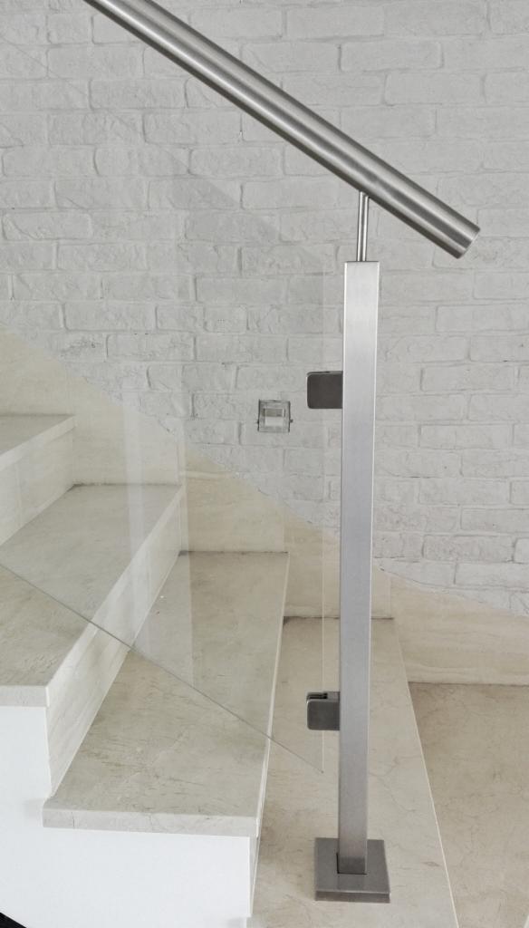 Szklana balustrada z elementami ze stali nierdzewnej, zamocowana do marmurowych schodów, na tle ściany z białej cegły.