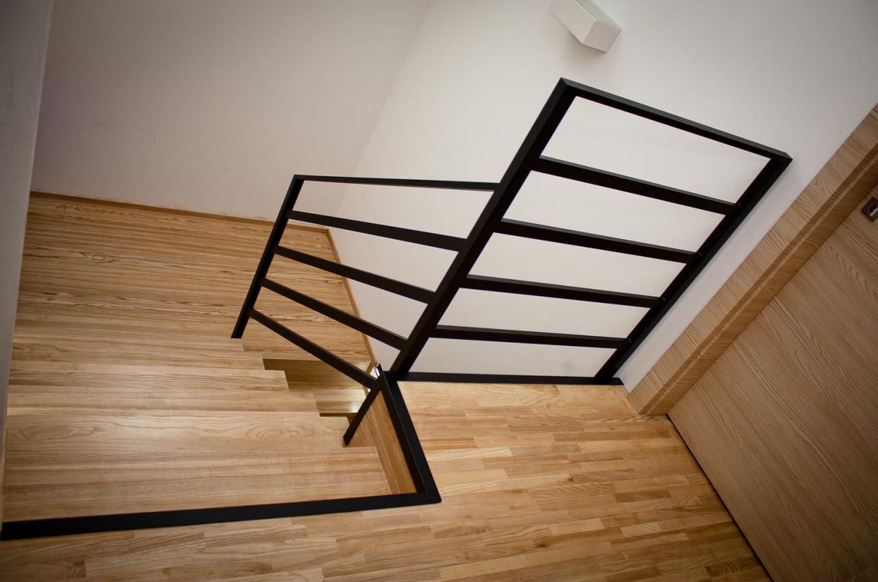 Nowoczesne schody drewniane z czarną metalową balustradą, widok z góry, jasne drewno i minimalistyczny design.