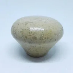 Polerowany, beżowy element dekoracyjny z porowatego kamienia, przypominający kształtem grzyba, na białym tle.