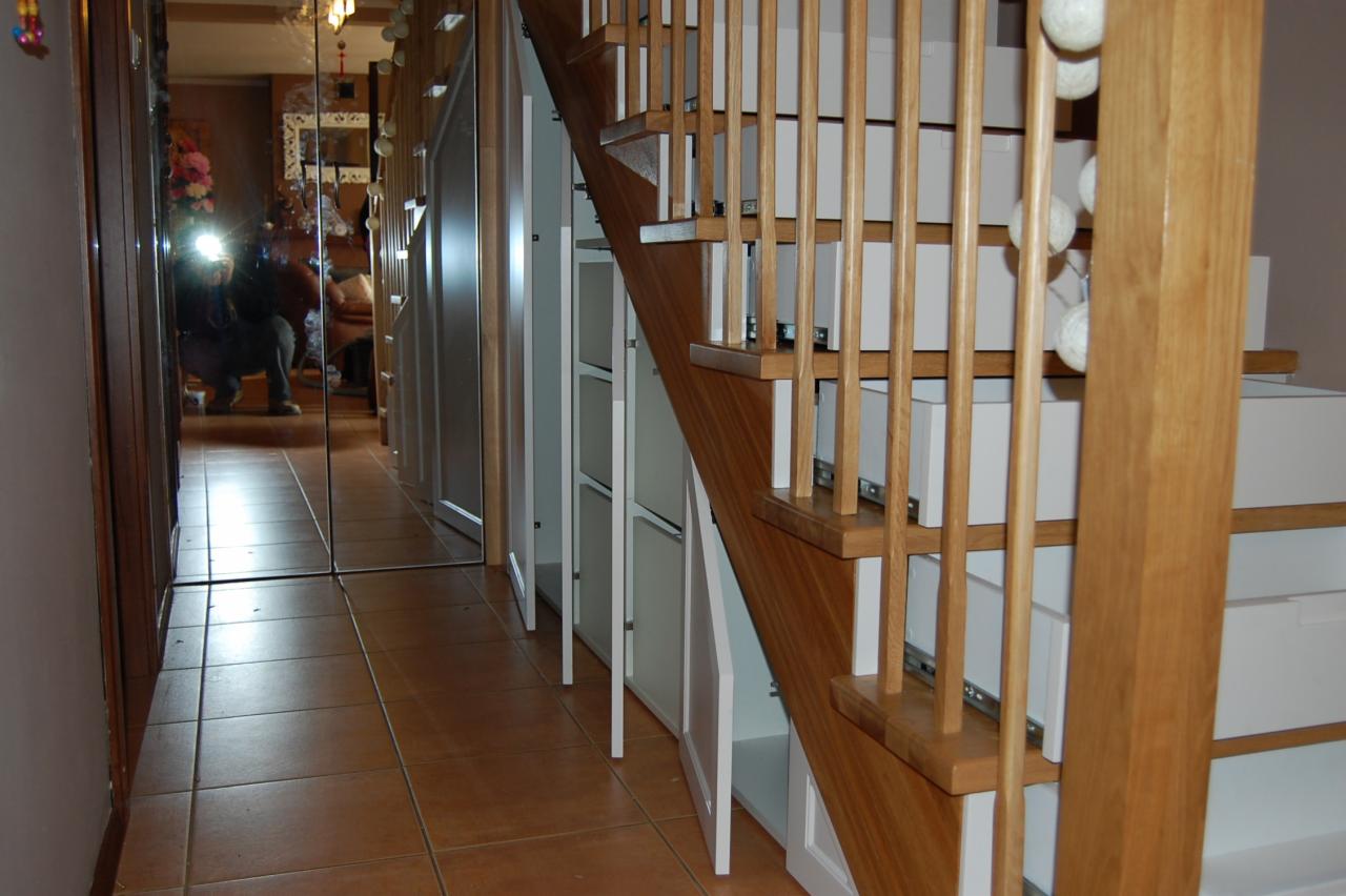 Schody z zabudowanymi szafkami i szufladami, drewniane barierki, brązowe płytki podłogowe, lustro odbijające wnętrze