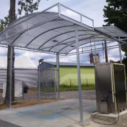 Zadaszenie nad stanowiskiem ładowania pojazdów elektrycznych, konstrukcja stalowa z przezroczystym dachem łukowym, widoczny automat do ładowania z kablem.