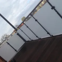 Balkon z balustradą z paneli mlecznego szkła i ciemnego metalu, widok z dołu na pochmurne niebo.