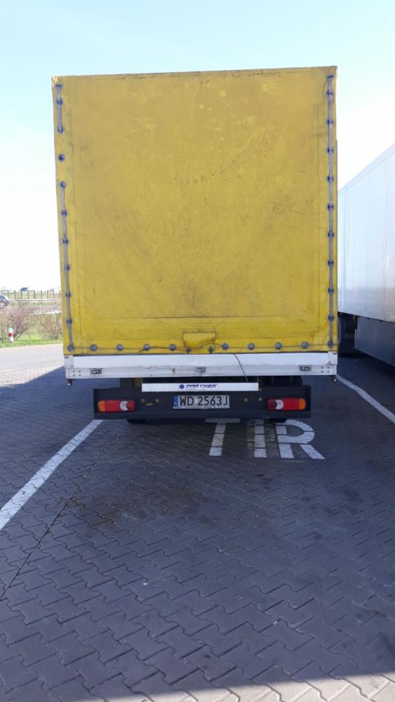 Tył żółtej naczepy ciężarówki zaparkowanej na brukowanym parkingu z napisem 'TIR', widoczna tablica rejestracyjna WD 2563J.