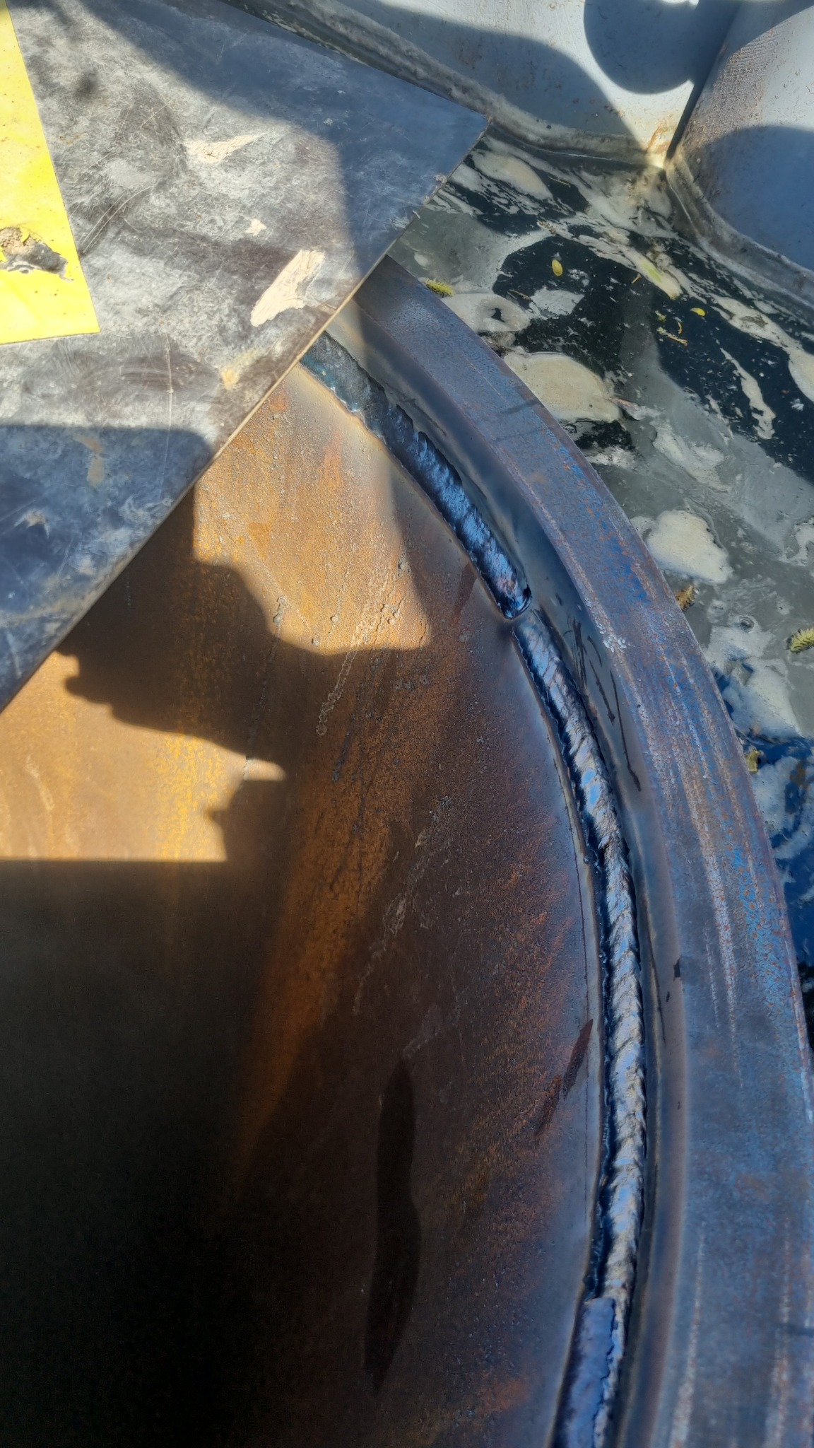 Spoina na styku blachy i rury. Widoczne ślady spawania, rdza i niedoskonałości powierzchni. Detal z procesu obróbki metalu.