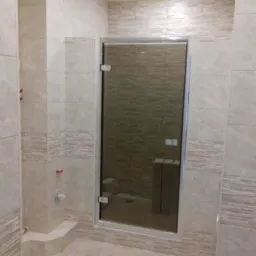 Wykończona łazienka z beżowymi płytkami imitującymi marmur i szklanymi drzwiami kabiny prysznicowej z chromowanymi zawiasami.