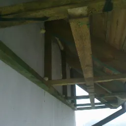 Widok od dołu na konstrukcję drewnianą dachu przy ścianie budynku, z widoczną pianką uszczelniającą między elementami, oraz rynną odprowadzającą wodę.