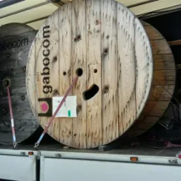 Dwie duże, drewniane szpule z kablami marki Gabocom, zabezpieczone pasami, przewożone w otwartej przestrzeni ładunkowej samochodu dostawczego.