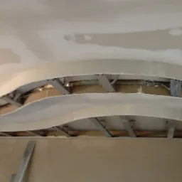 Sufit podwieszany z płyt kartonowo-gipsowych, z widoczną metalową konstrukcją nośną i wstępnym szpachlowaniem, w trakcie prac wykończeniowych.