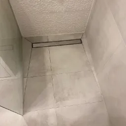 Nowoczesna kabina prysznicowa z szarymi płytkami, odpływem liniowym i heksagonalną teksturą na suficie.