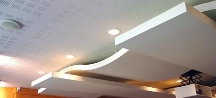 Nowoczesny sufit podwieszany z elementami dekoracyjnymi w kształcie fali, oświetlenie punktowe LED, perforowana powierzchnia sufitu głównego.