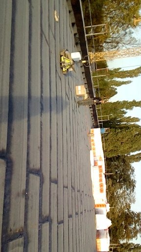 Prace na dachu z papy termozgrzewalnej, widoczny pracownik w oddali i sprzęt do zgrzewania papy.