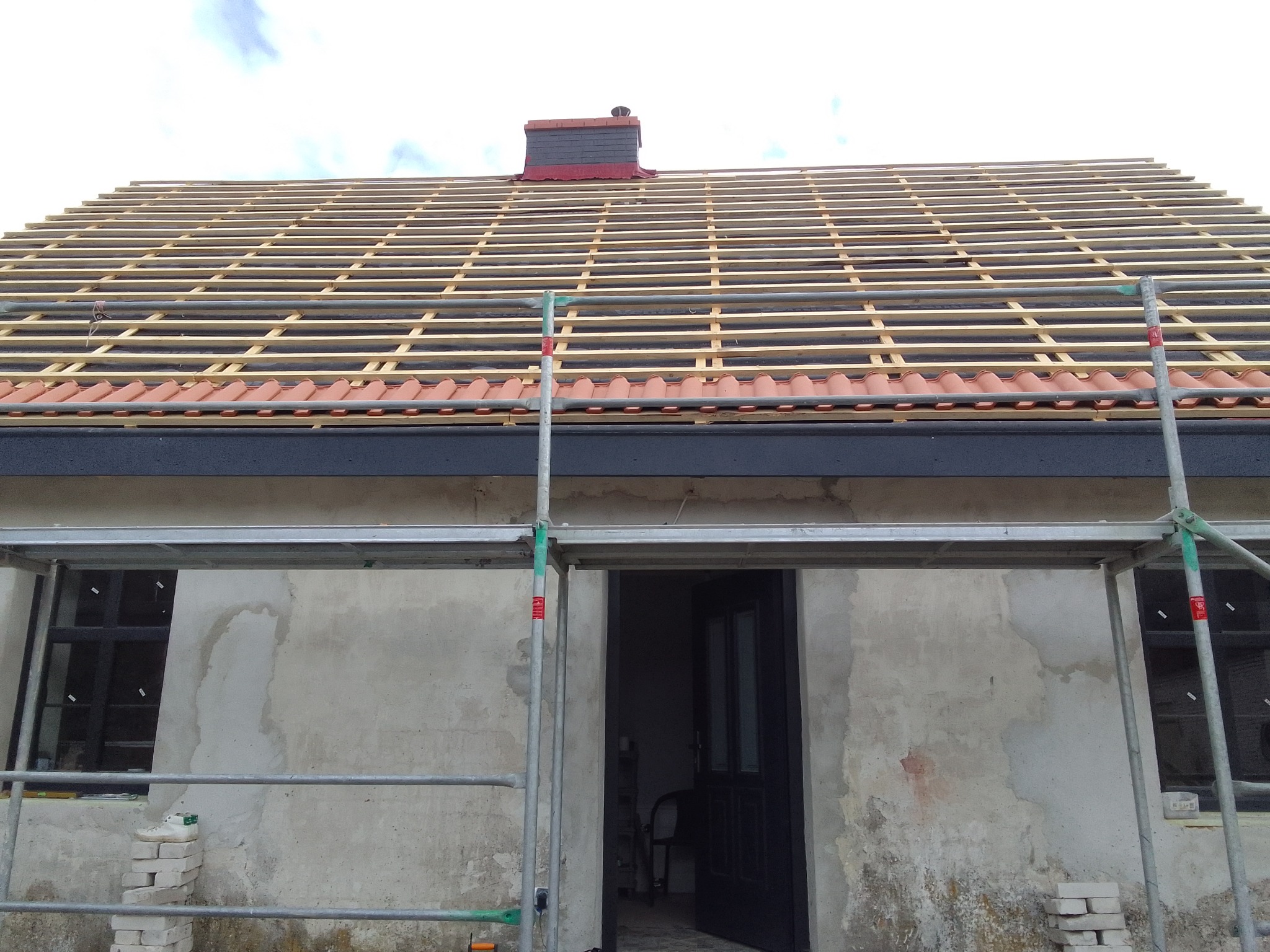 Budowa dachu: widok rusztowania przed domem z częściowo ułożoną dachówką i przygotowanym szkieletem dachu z łat i kontrłat.