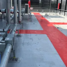 Szare, płaskie pokrycie dachu biurowca w Bydgoszczy z czerwoną hydroizolacją w formie pasów, widoczne elementy wentylacji i instalacji technicznej.