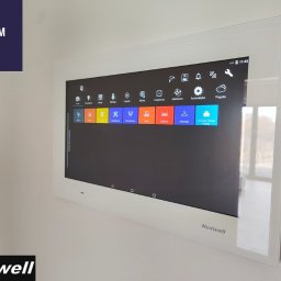 ELDAM Damian Szlendak - Biały panel dotykowy LCD 15,6 cala firmy Nexwell, zamontowany na ścianie, wyświetlający interfejs systemu smart home z ikonami różnych funkcji.