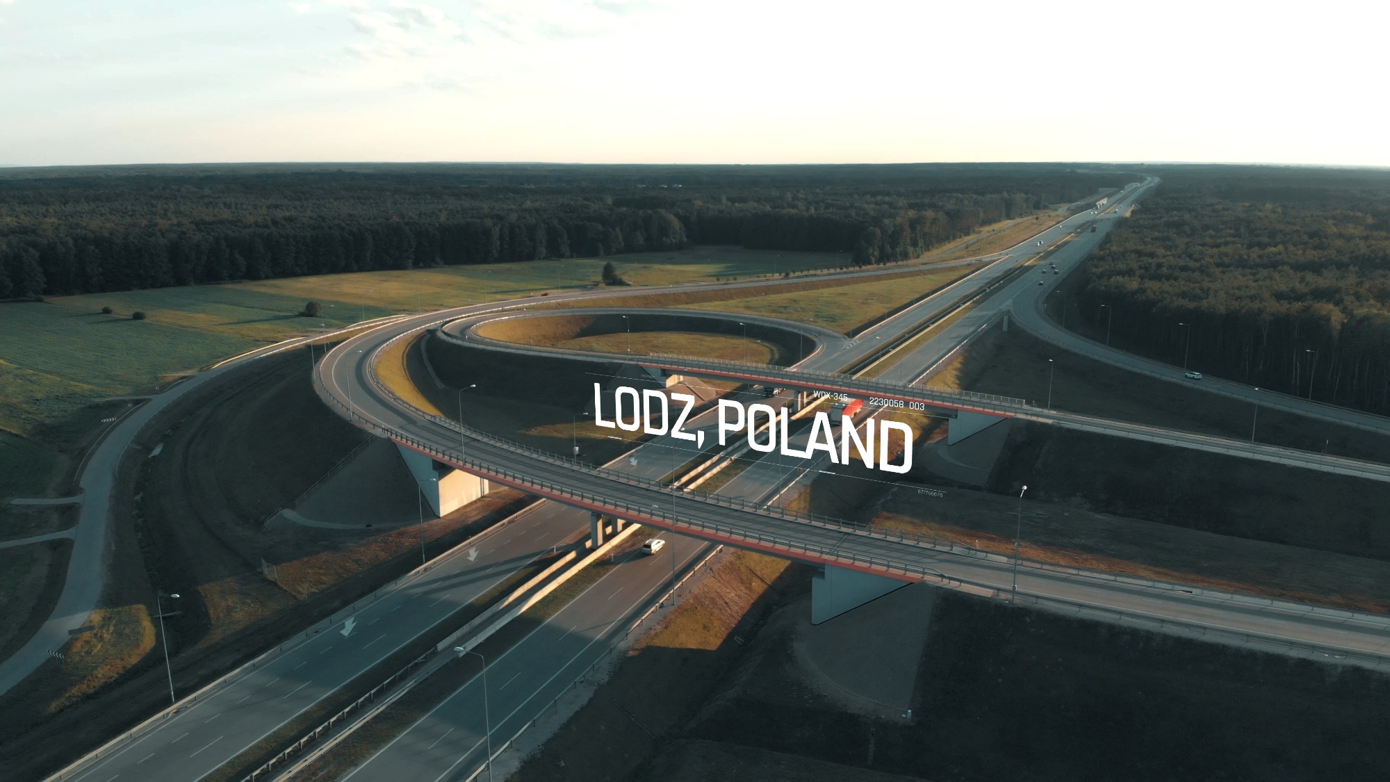 Panorama węzła drogowego w Łodzi z lotu ptaka, z widocznymi wiaduktami, drogami i otaczającym lasem.