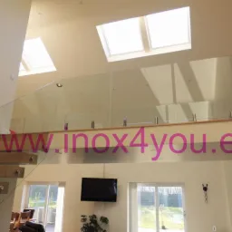 Dwupoziomowe wnętrze z drewnianymi schodami i szklaną balustradą zabezpieczającą antresolę, widoczne okna dachowe i salon z telewizorem.