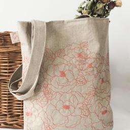 Pracownia Mantica - Lniana torba na zakupy z delikatnym haftem w kwiaty, umieszczona obok wiklinowego kosza i bukietu suszonych róż.