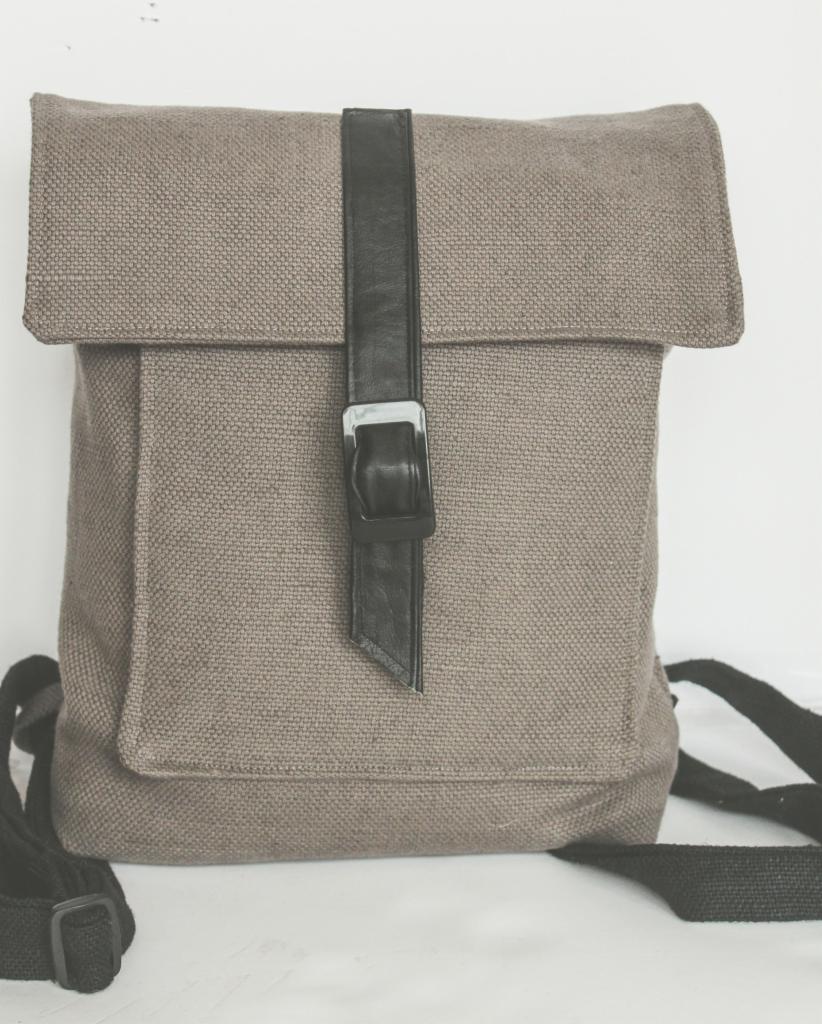 Lniany plecak w odcieniach szarości z czarnym, skórzanym paskiem zapinanym na klamrę, widoczne czarne paski naramienne.