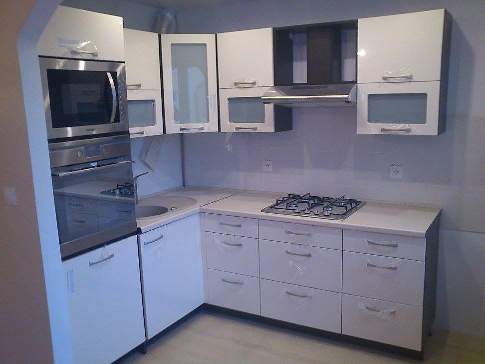 Biała kuchnia z lakierowanymi frontami, zabudowana pod sufit, z piekarnikiem i mikrofalówką w słupku, szklanymi wstawkami w górnych szafkach i płytą gazową na blacie.