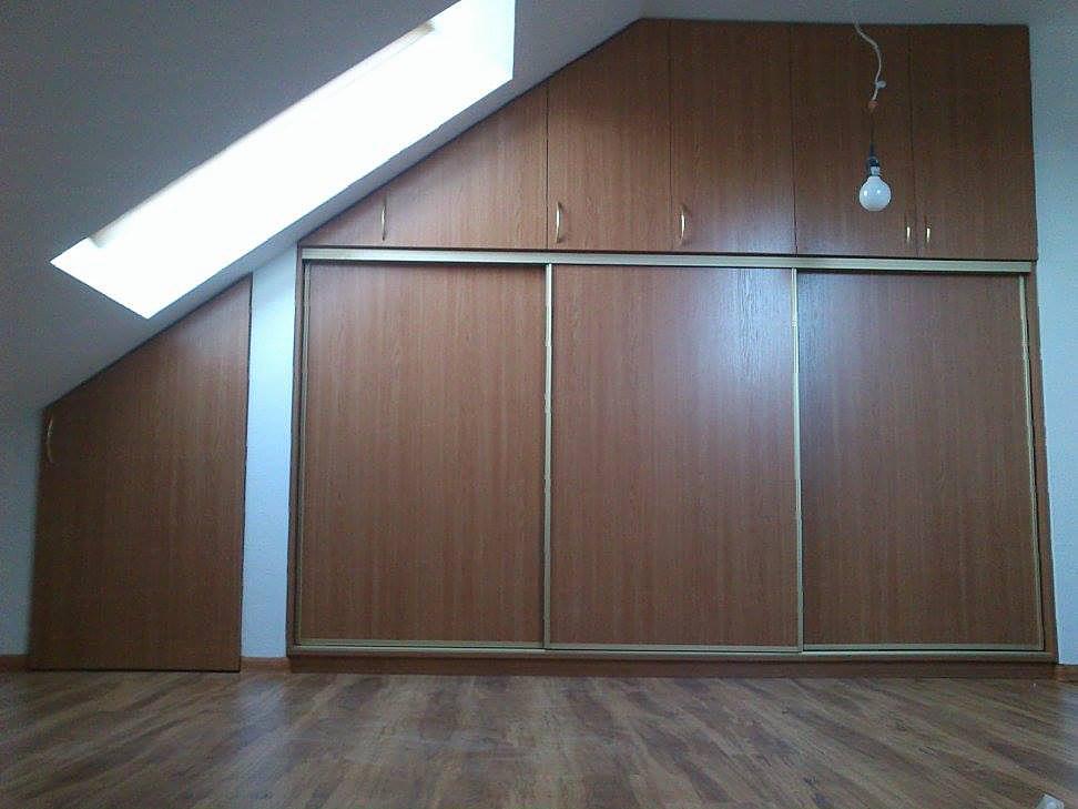 Szafa wnękowa z przesuwnymi drzwiami w odcieniach brązu, dopasowana do skosu poddasza, z górnymi szafkami i wiszącą żarówką na tle białej ściany.