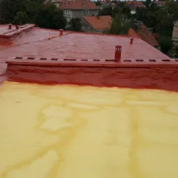 Czerwono-żółta powłoka na dachu budynku, widok z góry, w tle zabudowa miejska.