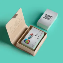 Stos wizytówek z kodem QR i danymi kontaktowymi w otwartym, tekturowym pudełku z wytłoczonym logo firmy na tle turkusowym. Elegancki minimalizm.