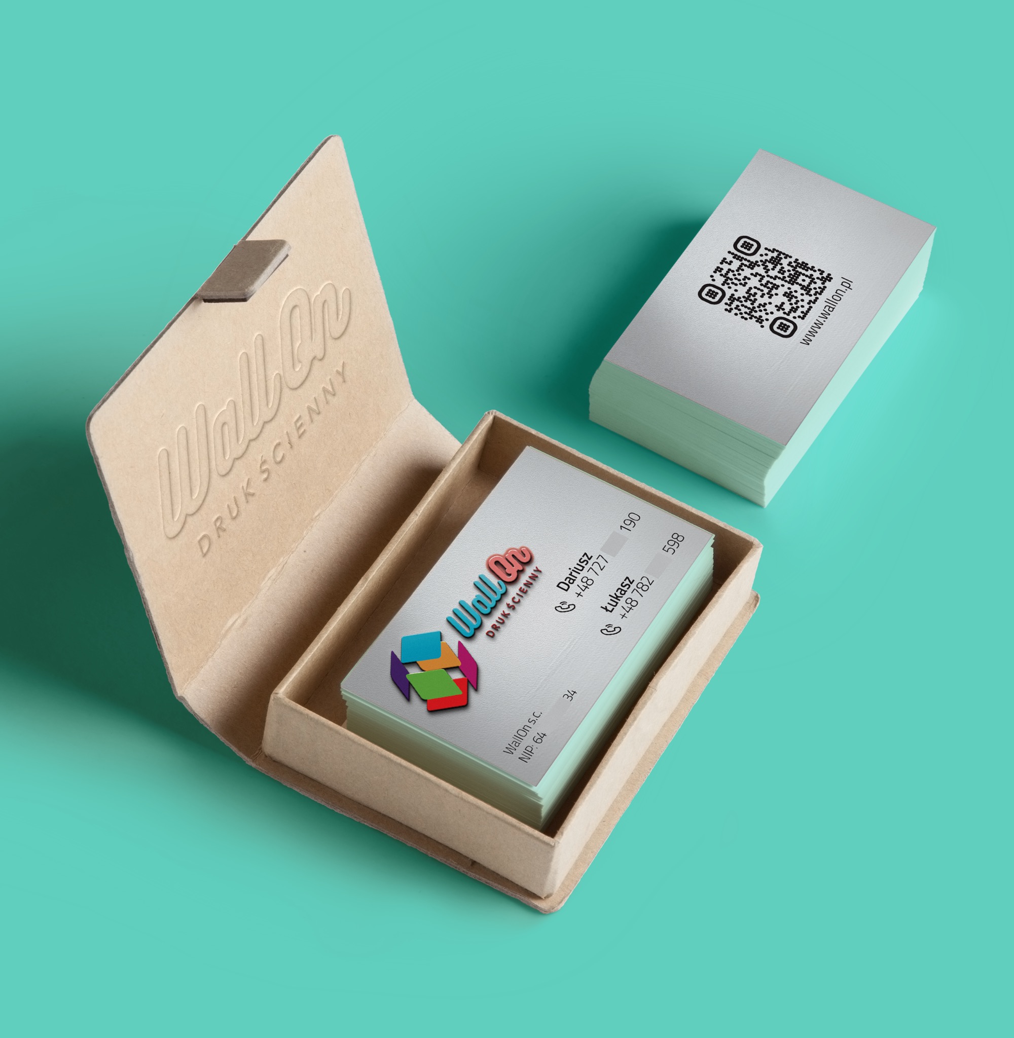 Stos wizytówek z kodem QR i danymi kontaktowymi w otwartym, tekturowym pudełku z wytłoczonym logo firmy na tle turkusowym. Elegancki minimalizm.