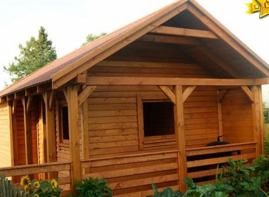 Drewniana altana z zadaszeniem, widok z zewnątrz, z elementami dekoracyjnymi i roślinnością w tle.