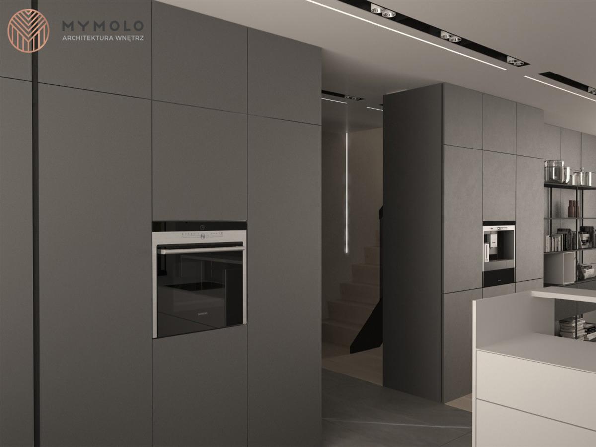 Szare matowe meble kuchenne na wymiar z wbudowanym piekarnikiem i ekspresem do kawy, minimalistyczne oświetlenie podszafkowe i schody w tle.