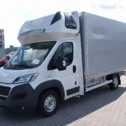 Biały samochód dostawczy z plandeką marki LAMAR na parkingu przed salonem samochodowym Fiat i Hyundai.