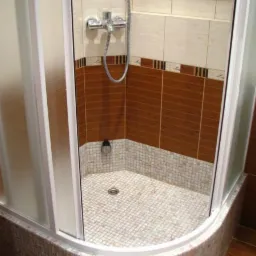 Kabina prysznicowa z mozaikową posadzką i brązowo-białymi płytkami na ścianach, chromowana bateria i wnęka w górnej części ściany.