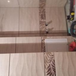 Usługi Remontowo-Budowlane - Ściana w trakcie wykańczania z beżowych płytek z motywem liści, widoczne krzyżyki dystansowe i narzędzia glazurnicze.