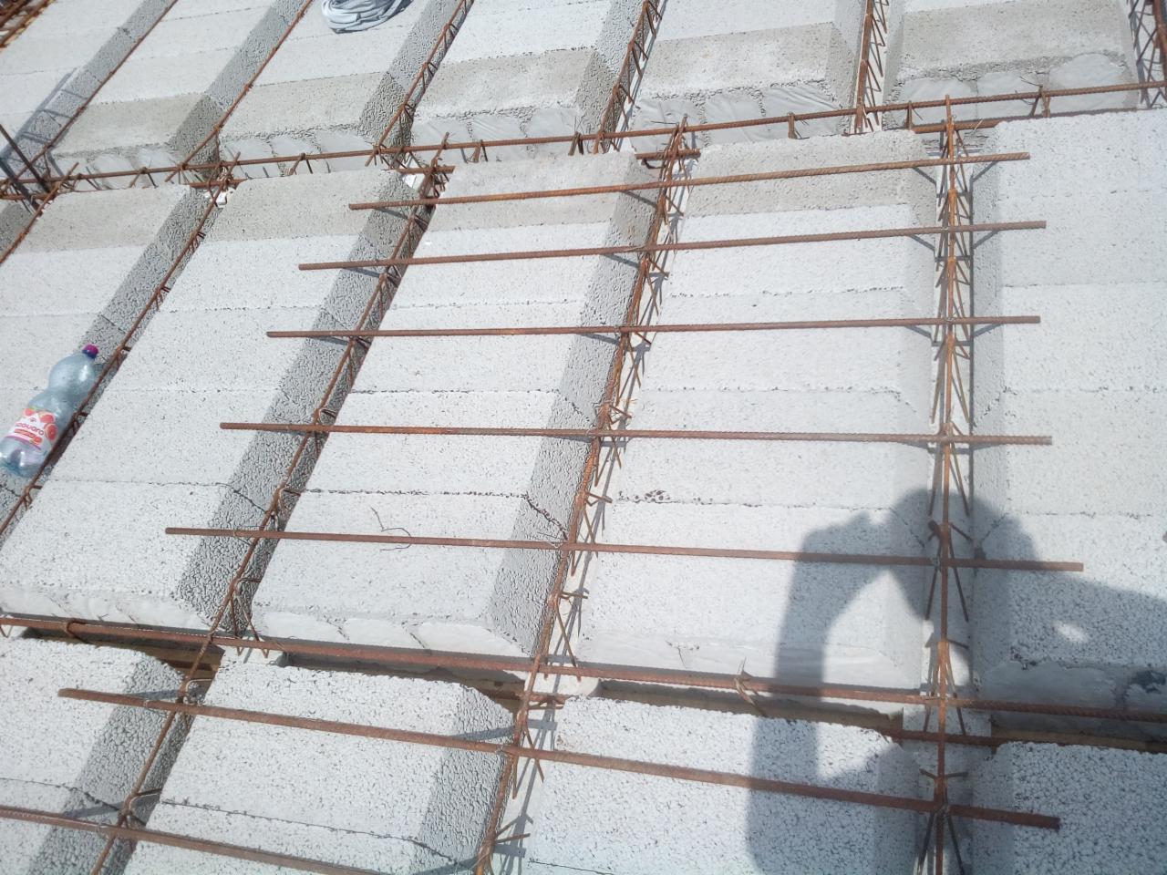 Konstrukcja stropu Teriva: betonowe pustaki i zbrojenie stalowe, widoczna butelka wody mineralnej po lewej stronie i cień osoby po prawej.